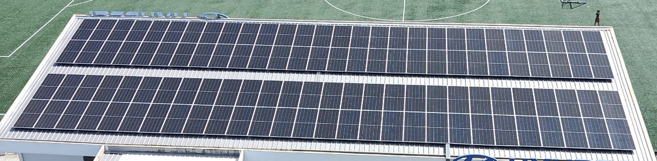 Paneles solares sobre techo de lámina junto a cancha de fútbol (vista aérea)